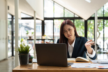 Fototapeta premium Young stressed businesswoman working at desk in modern office shouting at laptop screen and being angry about financial situation, jealous of rival capabilities, unable to meet client needs.