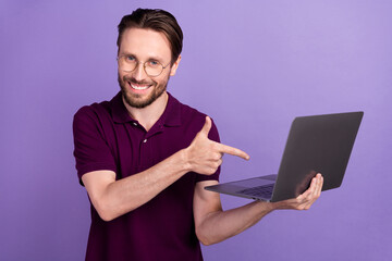 Photo of young cheerful man indicate finger laptop promo recommend ads isolated over violet color background