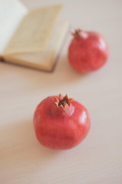 Two red ripe pomegranate and an open recipe book on a wooden table.