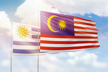 Sunny blue sky and flags of malaysia and uruguay