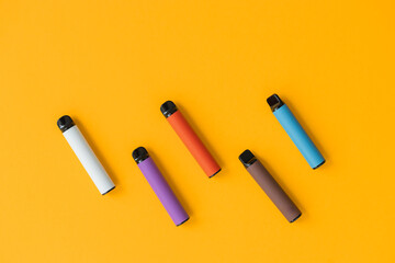 Modern disposable electronic cigarettes and word electronic smoking on yellow background