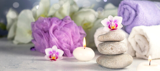 Fototapeta na wymiar banner with massage stones, burning candles, rolled towels, flowers, abstract lights. Spa resort therapy composition in lilac colors Soft focus