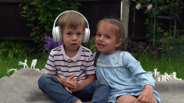Two Happy Siblings boy ans girl listening to music on headphones outside in Garden. Children and technology. Brother and Sister. Love of music, dreams hobbies. Childhood, musicality, hobby. Friendship