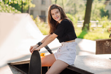 Fototapeta na wymiar Teenager skater girl with a skateboard sitting in the skaters park