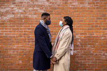 Fototapeta na wymiar Couple Wearing Face Masks Holding Hands by Brick Wall