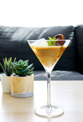 Homemade coffee martini cocktail in tall glass garnish with orange candy with mints set on wooden table in living room, drink at home concept. - obrazy, fototapety, plakaty