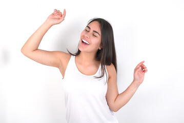 Photo of upbeat young beautiful brunette woman wearing white top over white wall has fun and dances carefree wear being in perfect mood makes movements. Spends free time on disco party