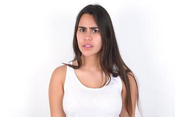 Portrait of dissatisfied young beautiful brunette woman wearing white top over white wall smirks...