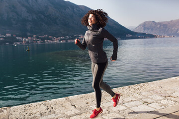 Female with curly hair runner jogging during outdoor workout on beach