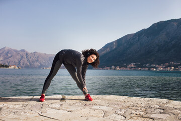 Athletic young woman with curly hair doing exercises on the beach