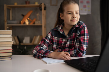 Homeschool using laptop. Caucasian little girl student learning virtual internet online class from school teacher by remote meeting. Schoolgirl watching lesson online and studying