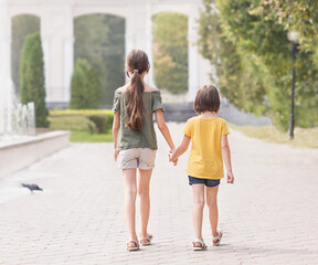 Vue arrière arrière deux petites filles de 7 et 9 ans portant des vêtements décontractés allant sur la pelouse verte du parc.