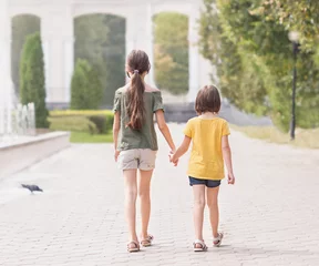 Foto op Plexiglas Achteraanzicht twee kleine meisjes van 7 en 9 jaar oud die vrijetijdskleding dragen die op het groene zonnegazon van het park gaan. © Albert Ziganshin