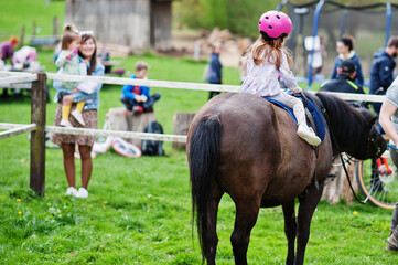 Small baby girl in pink helmet ride pony.