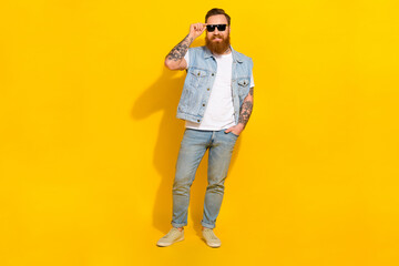 Fototapeta premium Photo of pretty cool man wear jeans waistcoat arm dark eyewear walking isolated yellow color background