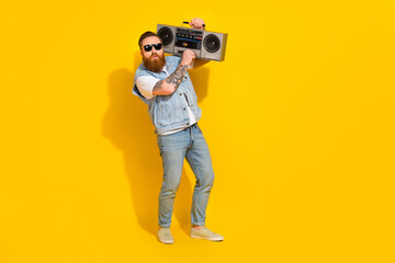 Photo of cute funny guy dressed denim vest rising dark glasses adjusting volume boombox empty space isolated yellow color background