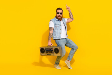 Photo of handsome cute guy dressed denim vest rising dark glasses listening boombox empty space isolated yellow color background