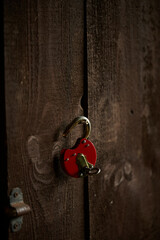 An open red padlock hung on an old wooden door