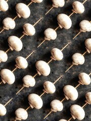 Background of champignons on a wooden skewer Mushroom pattern on a black concrete background. Vegetables to replace meat.
