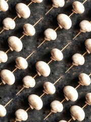 Background of champignons on a wooden skewer Mushroom pattern on a black concrete background....