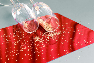 Festive Christmas New Year background with glassware. Two empty shiny glasses for wine and champagne on a table against a bright red silver background