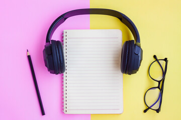 Black Headphone ,Eyeglasses,Notebook and Black pencil on pink and yellow background	