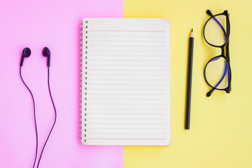 Notebook,Black pencil,Eyeglasses and Black Wired Earphones  on pink and yellow background
