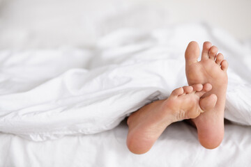 Wiggling toes of wakefulness. Shot of a pair of womans feet poking out from under the sheets of a...