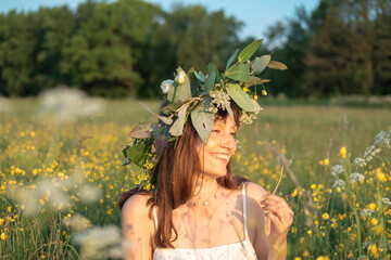 Woman with a flower wreath on her head and blows on a dandelion.