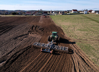 Obraz premium Tractor with cultivator plowing field. Tractor disk harrow on ploughing a soil. Planting in farmland. Sowing seed on plowed field. Seeding in agriculture. Farm Machinery for cultivating. Tractor plow.