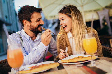 Young couple sitting in a restaurant eating pizza outdoor.