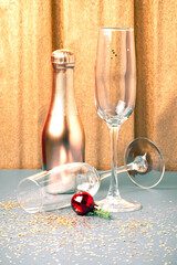 Festive golden silver Christmas New Year background with glassware. Two empty shiny wine glasses and a bottle of champagne on the table