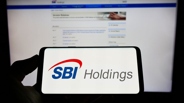 Stuttgart, Germany - 06-12-2022: Person holding cellphone with logo of Japanese financial company SBI Holdings on screen in front of business webpage. Focus on phone display.