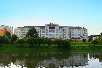 Fototapeta na wymiar River on sunrise. Townhouses buildings and multi-floor home at waterfront. Morning on River in city. Suburb houses and residential building near river in Minsk. House in nature on shore on sunset..