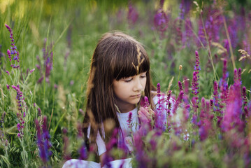 Cute little girl 7-8 years old, sitting in the lavender field, looking at the flowers