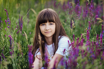 Pretty girl 7-8 years old, sitting in the lavender field, looking at the camera