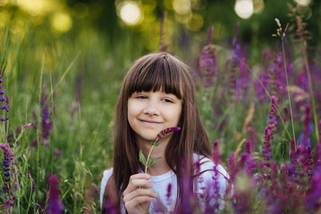 Cute happy girl 7-8 years old, sitting in the lavender field, smiling