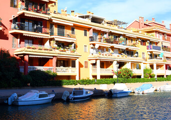 Fototapeta na wymiar Jetty with yacht. Yachts and motor boats in marina Port Saplaya, Valencia. Yacht and fishing motorboat in yacht club. Colourful houses with apartments at coast Mediterranean Sea. Sailboat near pier.
