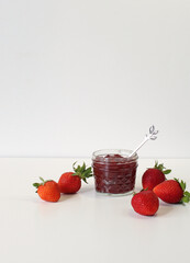 Homemade strawberry preserves or jam in a mason jar surrounded by fresh organic strawberries. Selective focus with white background.