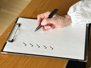 クリップボードに挟んだ白い紙にチェックする高齢女性の手元