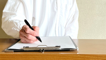 クリップボードに挟んだ白い紙に記入する高齢女性の手元_正面