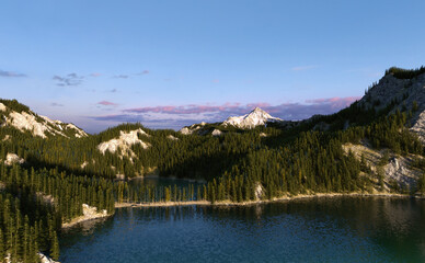Lake surrounded by mountains with snow and fir trees at sunrise. Aerial view. 3D render.