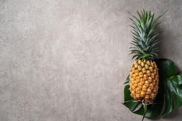 Fresh pineapple with tropical leaves on gray background.