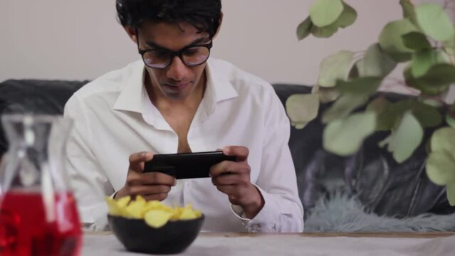 Young man playing games on his phone while snacking on crisps
