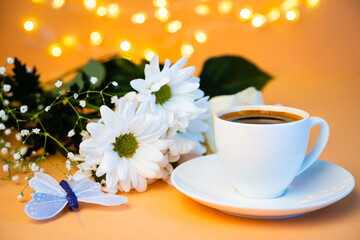 Scena still life con una tazzina di caffè e con un mazzo di fiori bianchi acanto e con una farfalla lillà su sfondo arancione con luci sfuocate sullo sfondo. Natura morta. Invito. 