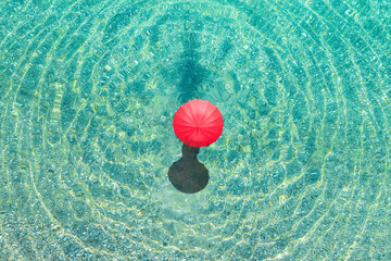 Top view of woman with red summer umbrella walking in tropical blue, turquoise transparent water...