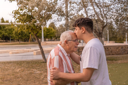 Nieto besando a su abuelo en el parque, con expresión cariñosa. Fotografía horizontal con espacio para texto.