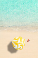 Aerial view of yellow umbrella, flip flops on sandy beach. Summer and travel concept. Blue, turquoise transparent water surface of ocean, sea, lagoon. Aerial, drone view. vertical