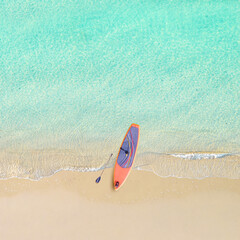 Top view of tropical Seychelles sand beach with SUP board for surfing on the shore. Blue, turquoise transparent water surface of ocean, sea, lagoon. Horizontal background. Aerial, drone view