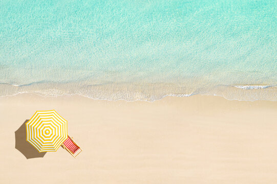 Aerial view of wooden sunbed, lounge, yellow umbrella on sandy beach. Summer and travel concept. Blue, turquoise transparent water surface of ocean, sea, lagoon. Aerial, drone view